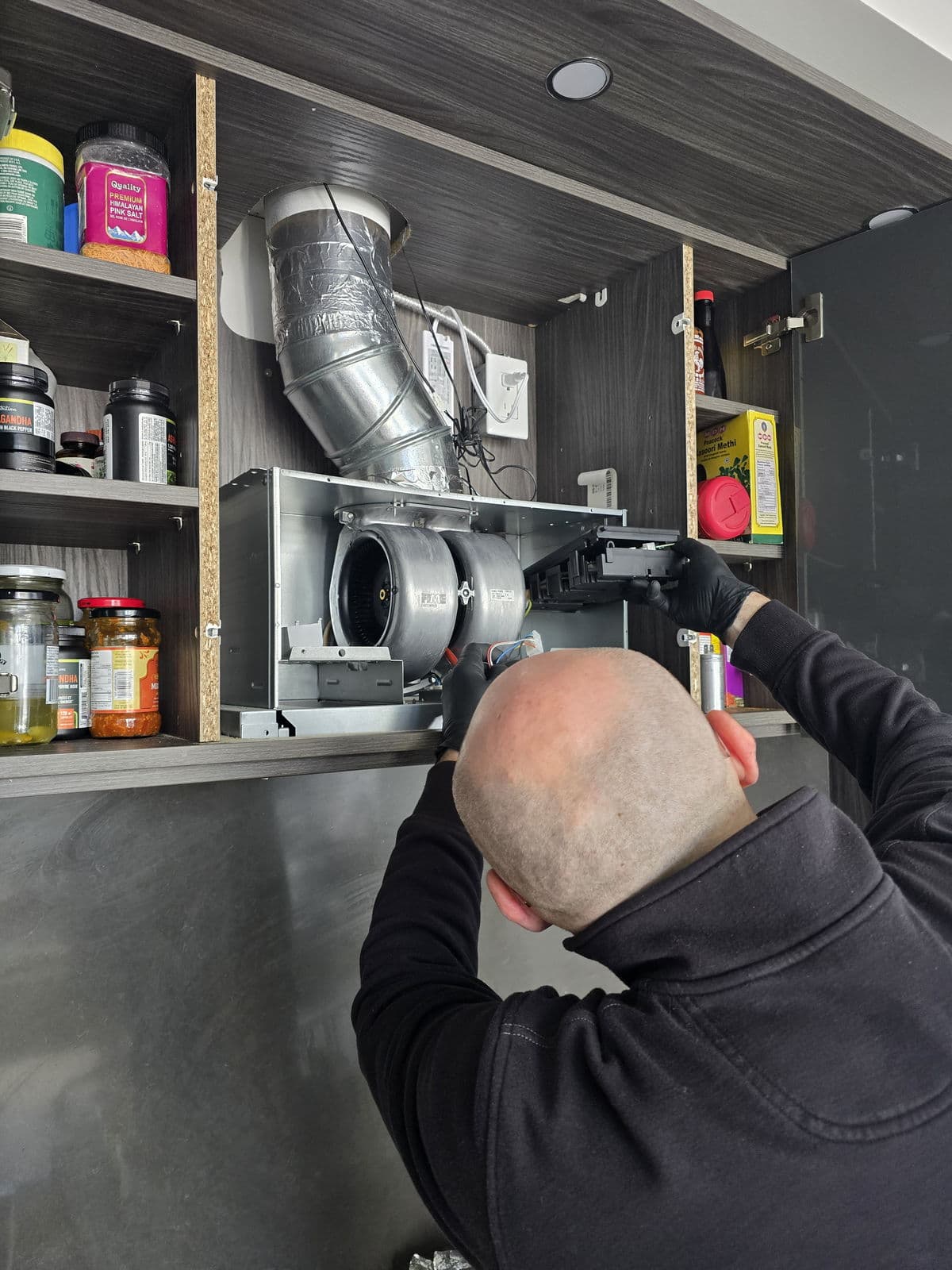 Technician repairing a range hood inside a kitchen cabinet
